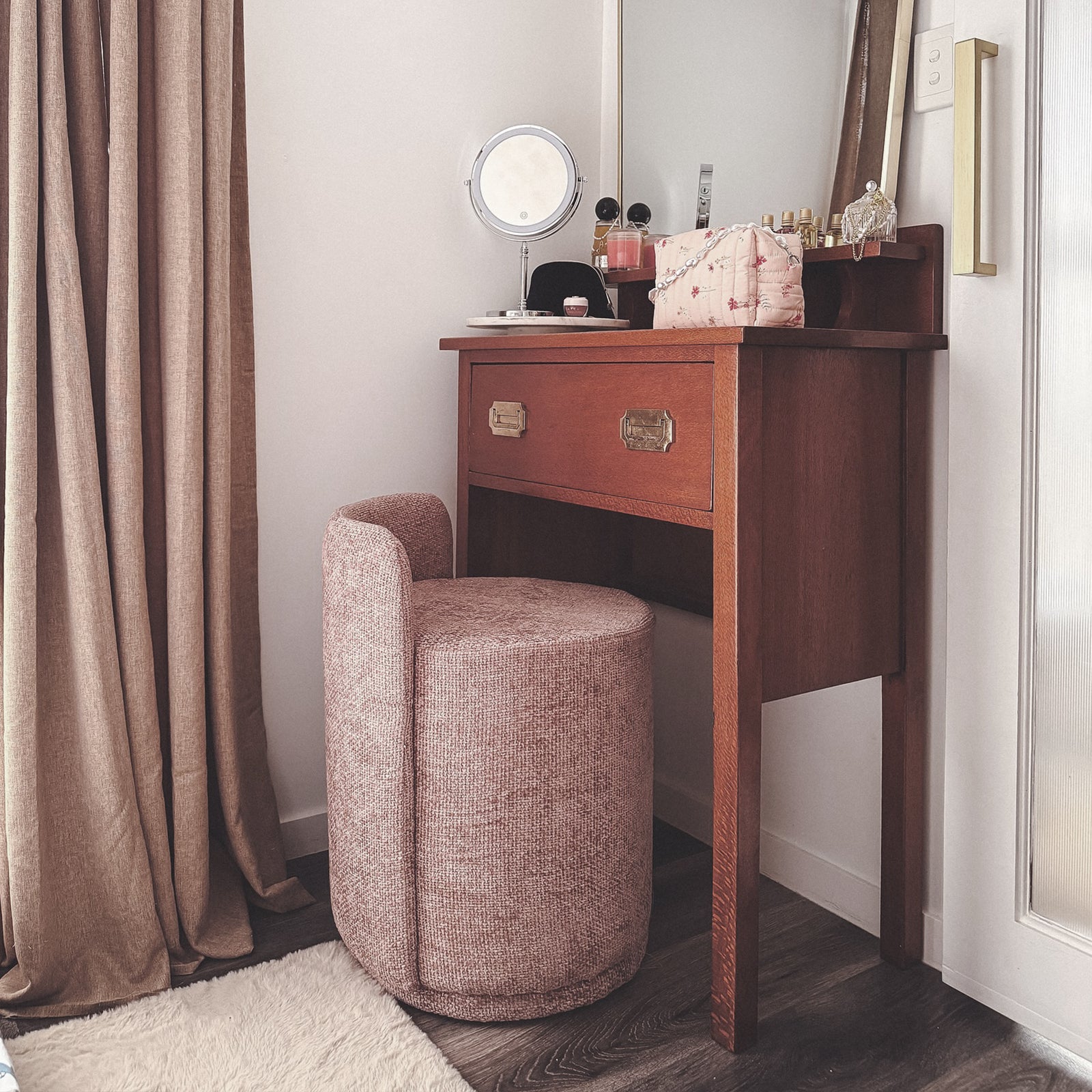 Hiboa Chenille Ottoman Stool in Light Pink, upholstered in ultra-soft chenille, tucked under a compact wooden vanity. Complements a luxurious dressing area with a plush, muted rose fabric.