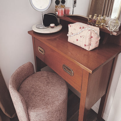 Hiboa Chenille Ottoman Stool in Light Pink alongside a wooden vanity, featuring a light-up mirror, makeup items, pink candles, small perfume bottles, and a jewelry dish, creating a luxurious dressing area.