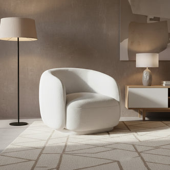 Janelle Bouclé Curved Accent Chair in White, featuring a rounded design, premium bouclé upholstery, and placed on a geometric-patterned rug, alongside a black floor lamp and a light wood side console.