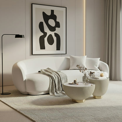 Janelle 213cm Curved Bouclé 3.5-Seater Sofa in Cream White, featuring plush throw pillows, a beige knitted blanket, and a solid wood frame, set in a minimalist living area.