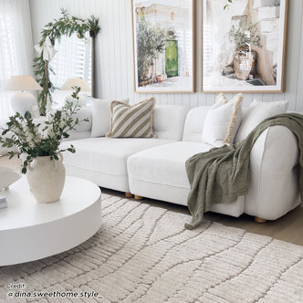 Kaelyn 3 Seater Modular Boucle Sofa with Pillows in Cream, featuring a textured boucle fabric, low-profile design, and coordinating olive green throw and pillows, set in a serene, Scandinavian-inspired living room corner.