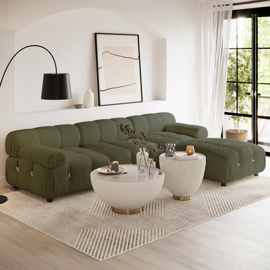 Keila 3 Seater Modular Tufted Boucle Sofa Set in Green sits in a minimalist living room corner, complemented by ribbed-ceramic coffee tables, an ivory textured rug, and a black arched lamp.