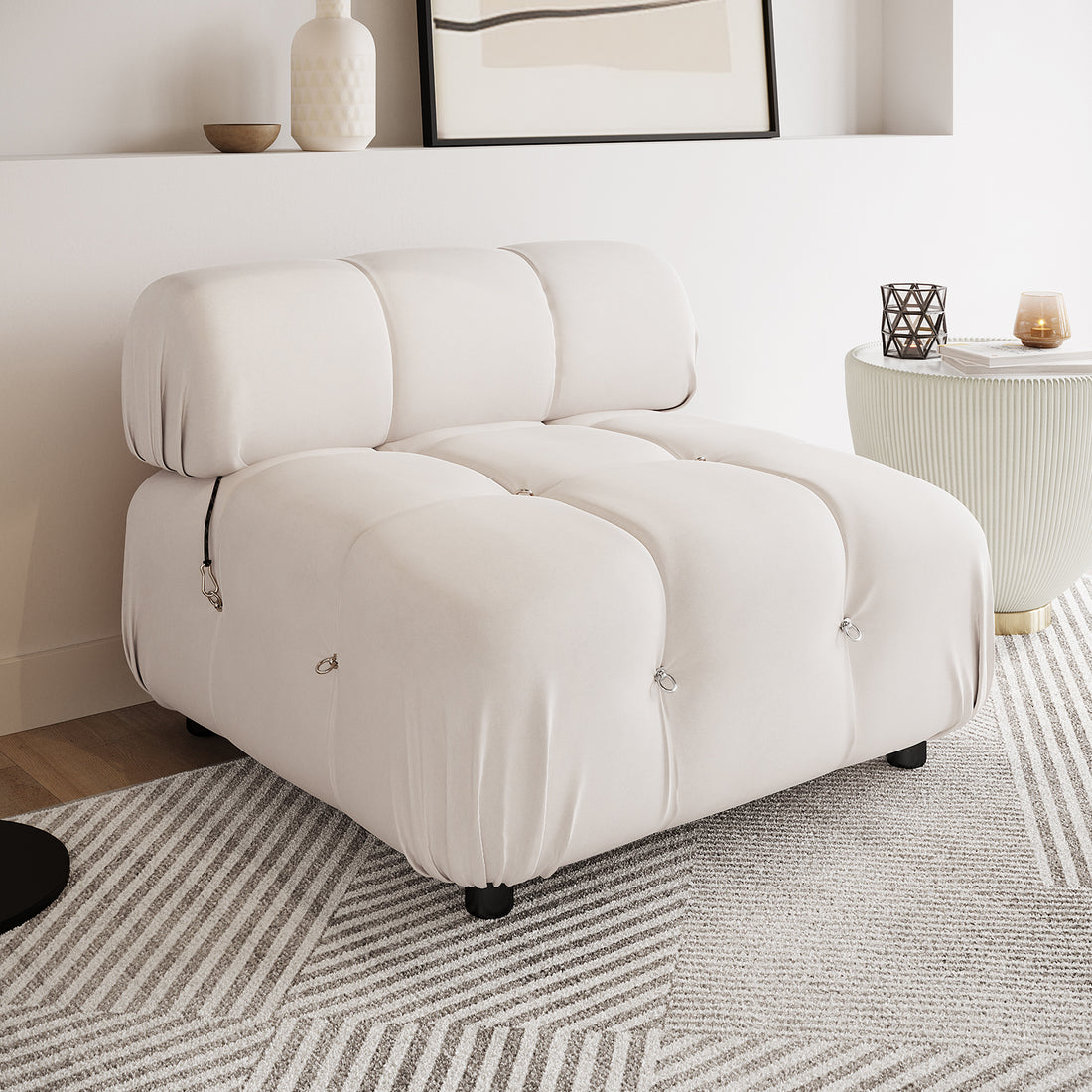 Keila Modular Tufted Single Sofa in Cream Velvet, featuring square tufted cushions with metal loops, sits on short black legs atop a patterned rug, exuding a modern and minimal aesthetic.