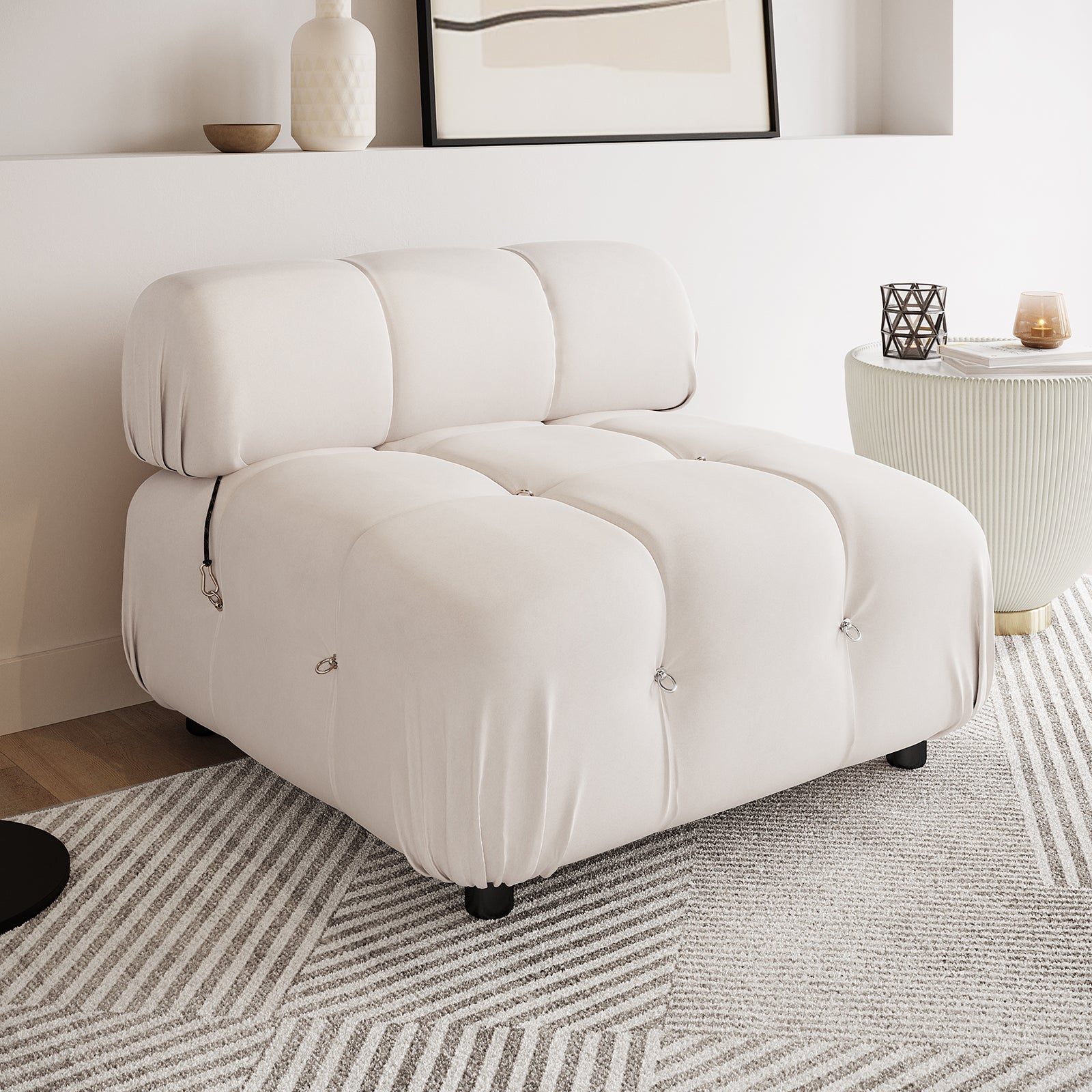 Keila Modular Tufted Single Sofa in Cream Velvet, featuring square tufted cushions with metal loops, sits on short black legs atop a patterned rug, exuding a modern and minimal aesthetic.
