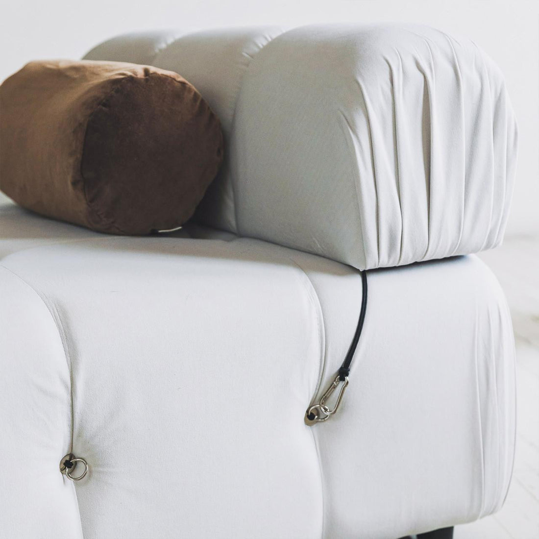 Close-up of the Keila Modular Tufted Single Sofa in Cream Velvet, showcasing its tufted design with a cylindrical brown bolster pillow and a black cord with a metal clip on a tufting ring.