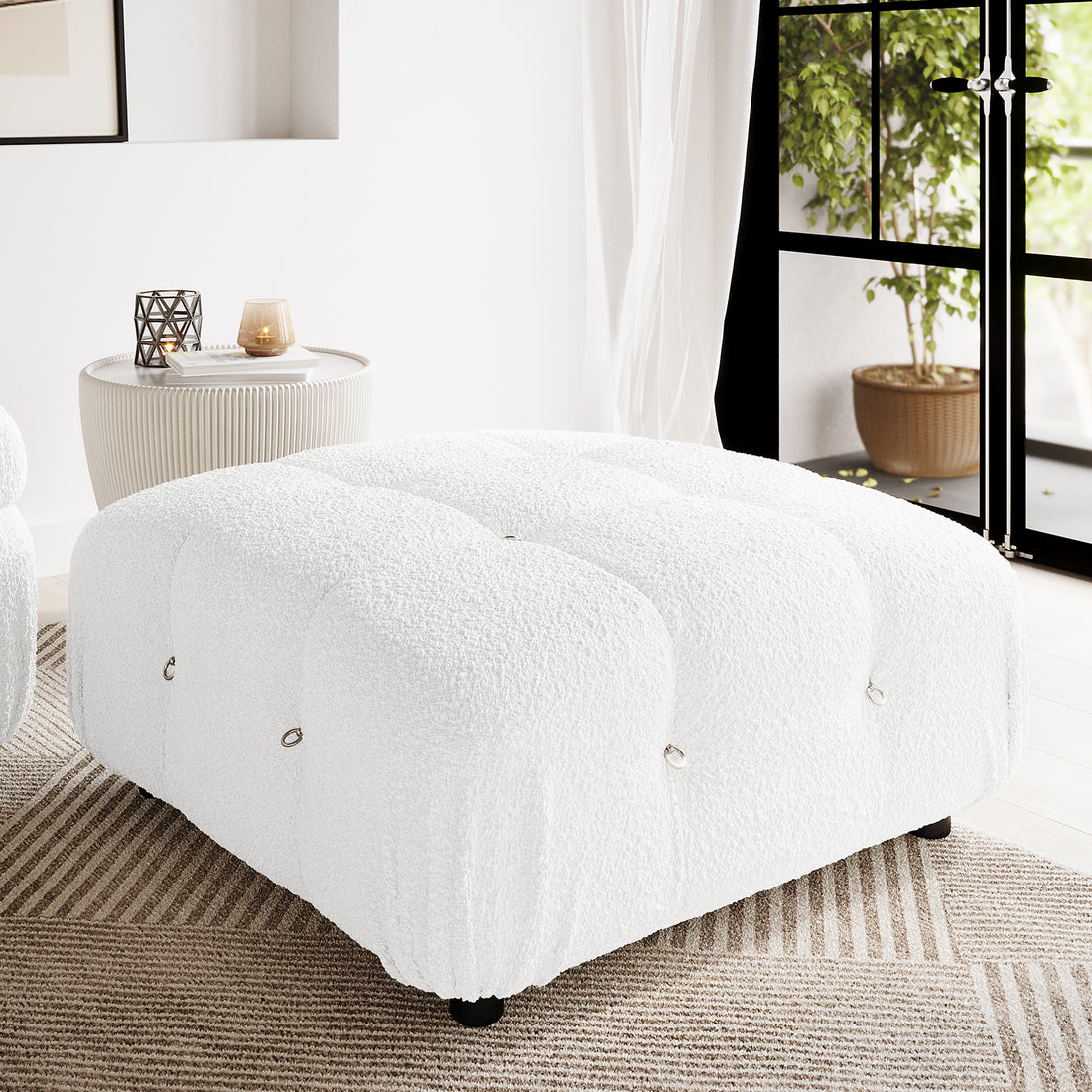 Keila Modular Tufted Boucle Ottoman in Cream White, featuring tufted channels and metal ring accents, placed on a neutral rug in a minimalist living room with a ribbed side table and sheer curtains.