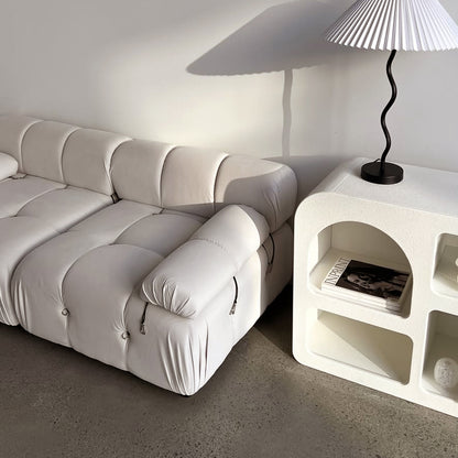 Keila 2 Seater Modular Tufted Sofa Set in Cream Velvet with tufted cushions and exposed zippers, next to a textured side unit holding magazines and a lamp, on polished concrete floor.