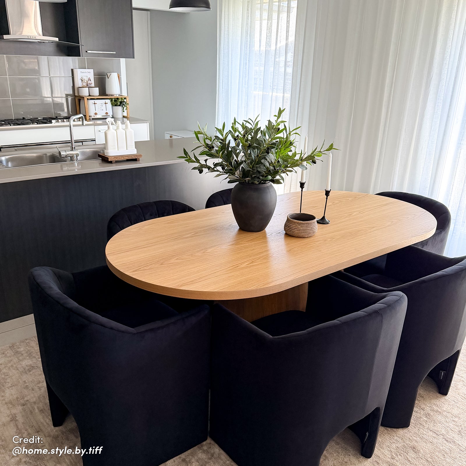 Liora Velvet Curved Accent Armchair in Black, positioned in a modern dining-kitchen area, showcases its sculptural silhouette and plush velvet texture amidst sleek, contemporary furnishings and decor.