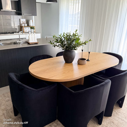 Liora Velvet Curved Accent Armchair in Black, positioned in a modern dining-kitchen area, showcases its sculptural silhouette and plush velvet texture amidst sleek, contemporary furnishings and decor.