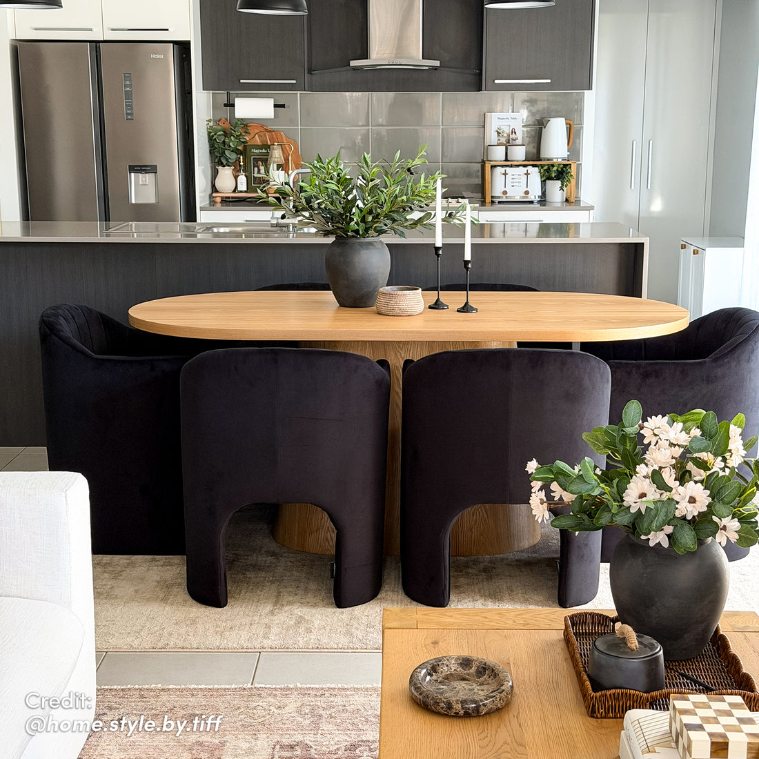 Liora Velvet Curved Accent Armchair in Black, featuring a sculptural silhouette with a high back and wraparound arms, sits elegantly in a bright kitchen-diner, adding sleek comfort to the modern space.