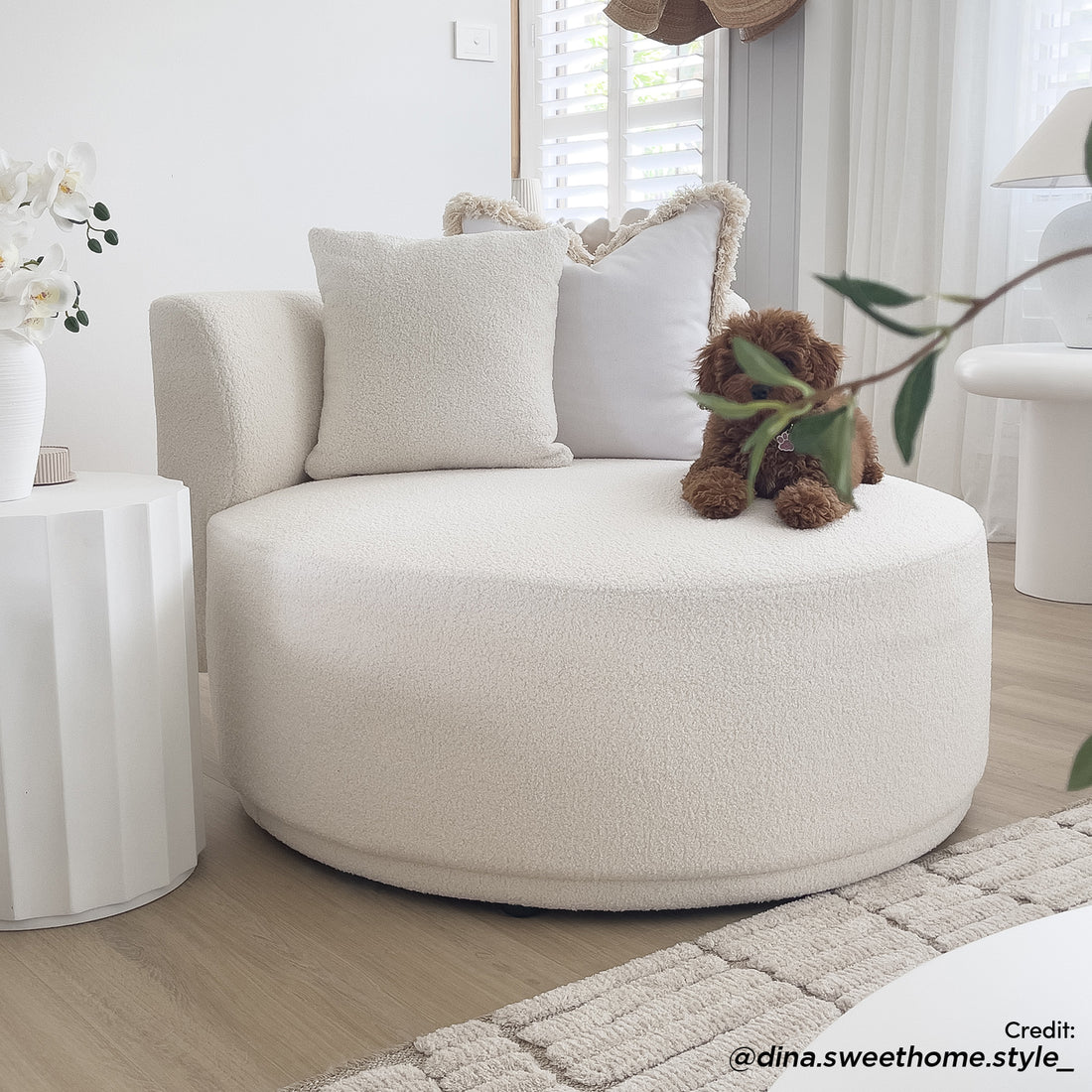 Lyana Single Seater Bouclé Sofa in Cream White, featuring a round design with bouclé upholstery, a fluffy throw pillow, and a textured cushion, complemented by a white side table with orchids.