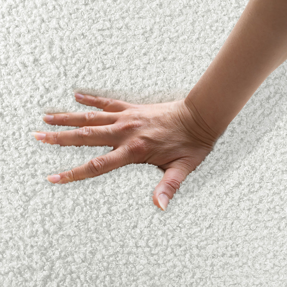A woman's hand presses into the plush, bouclé fabric of the Lyana 4 Seater Bouclé Sofa with Right Chaise in Cream White, showcasing its luxurious texture and comfort.
