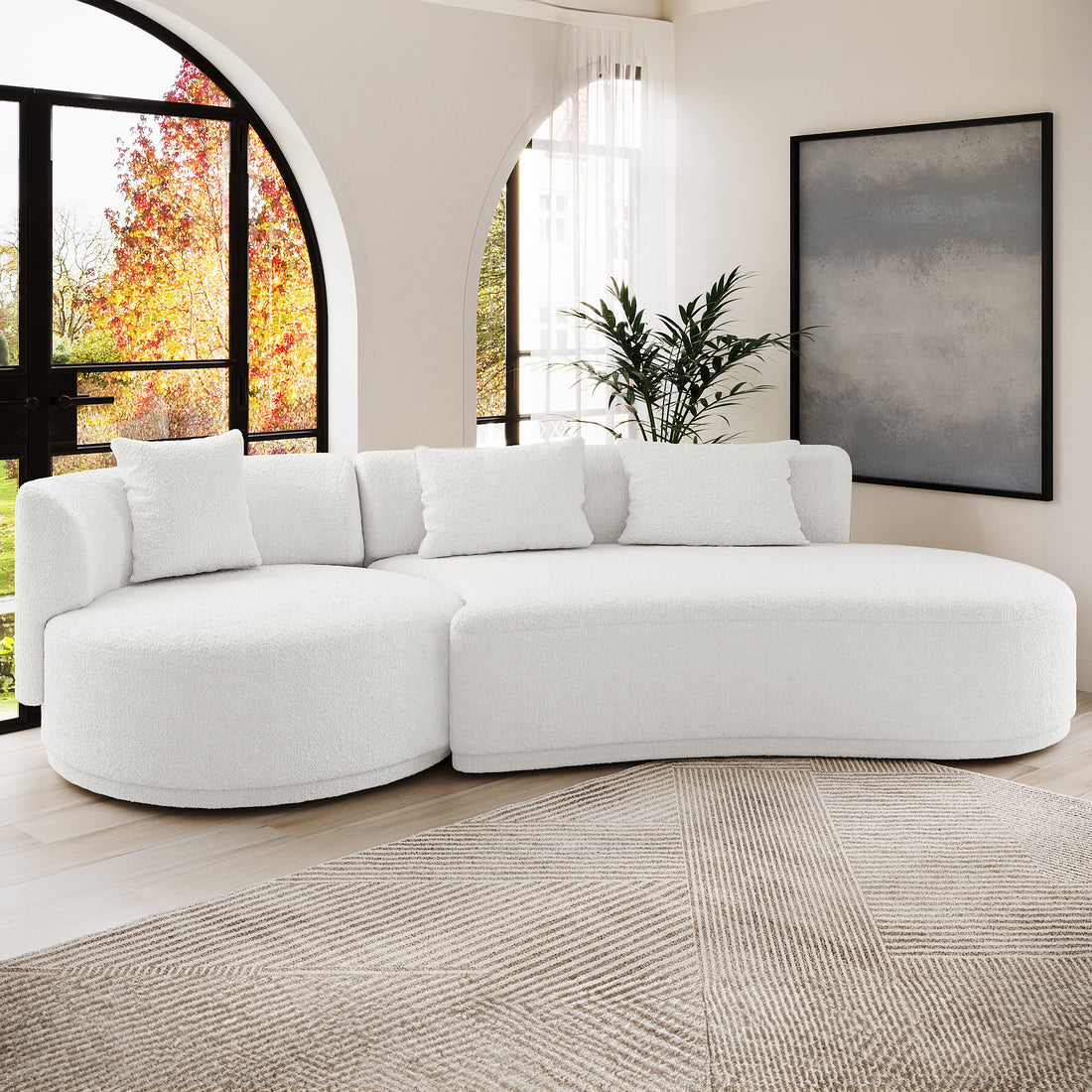 Lyana 4 Seater Boucle Sofa with Right Chaise in Cream White, featuring plush bouclé fabric, matching throw pillows, and curved design, set against arched windows with sheer white curtains and a large abstract painting.