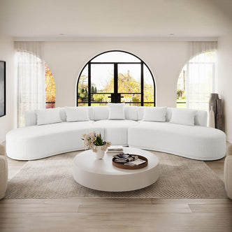 The Lyana 7 Seater Boucle Sofa Set in Cream White features a plush, curved design with matching throw pillows, set against arched windows, creating a serene, minimalist living room ambiance.