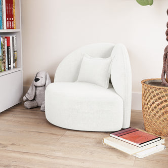 Mahsa Boucle Kids Sofa with Pillow in Cream White nestled in a cozy nook, paired with a plush stuffed animal, a book stack, and surrounded by bookshelves and a tall plant.
