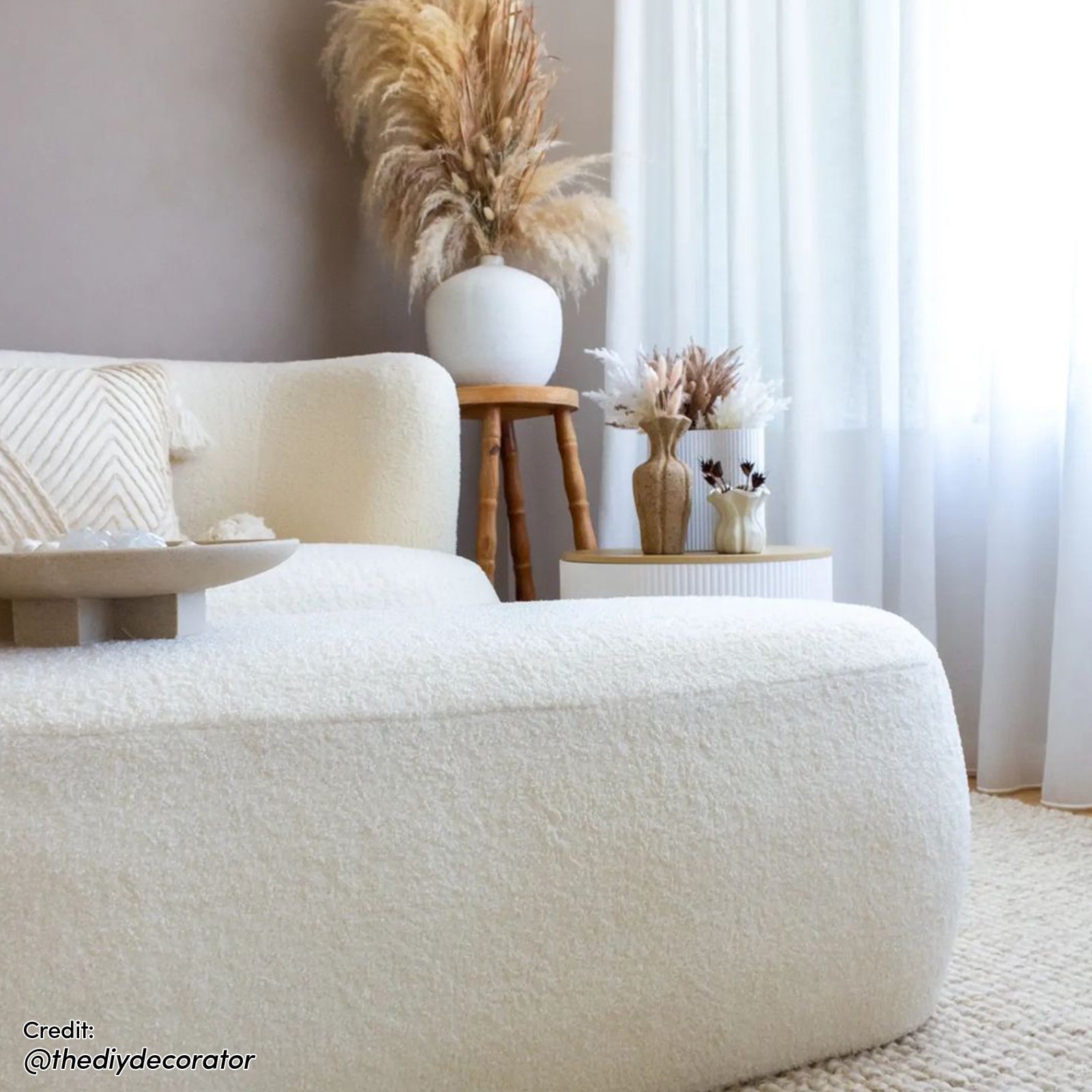 Massie 2-Seater Boucle Sofa in Cream White, upholstered in creamy boucle fabric, features a rounded design, matching throw pillow, and decorative bowl, set in a serene, modern-boho living room corner.