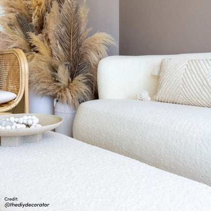 Massie 2-Seater Boucle Sofa in Cream White, featuring plush boucle fabric and a curved design, is styled in a neutral-toned living room with a matching ottoman and natural accents.