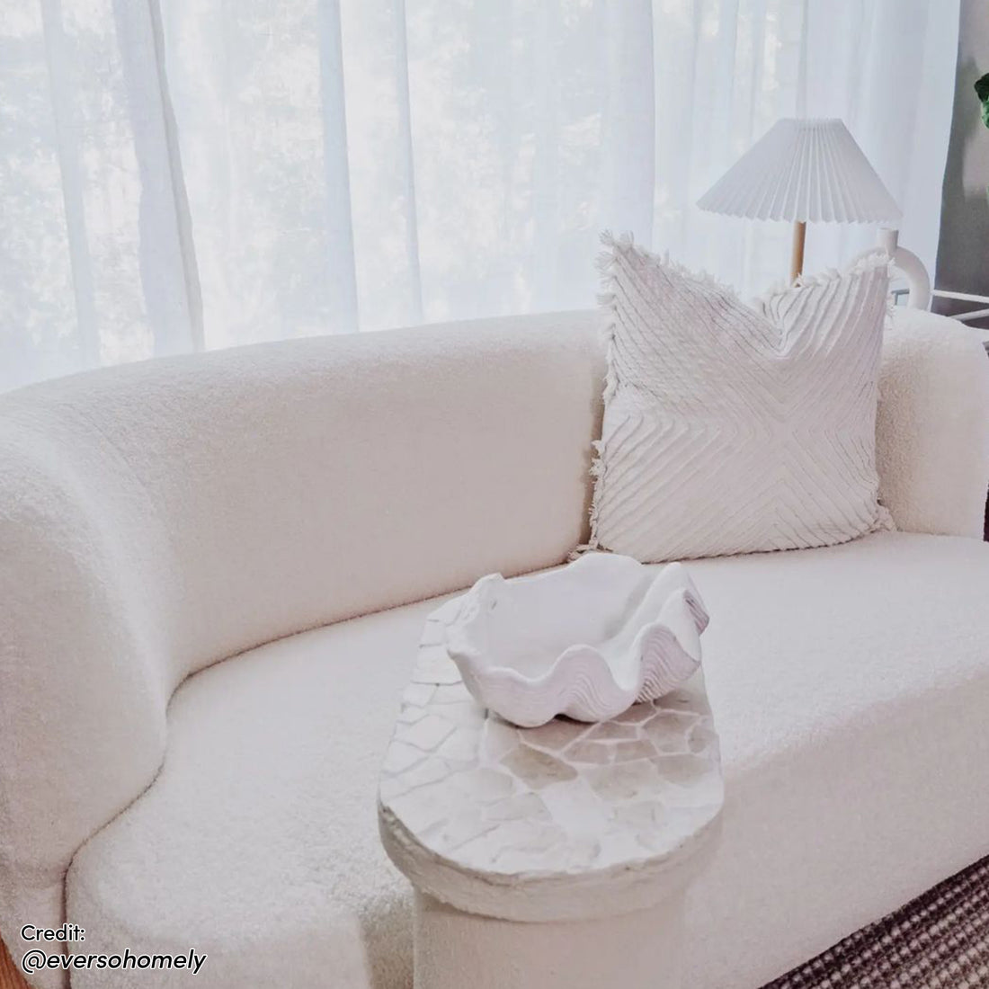 Massie 2-Seater Boucle Sofa in Cream White with softly curved design, featuring a cream throw pillow, built-in mosaic side table, and shell-inspired ceramic bowl, set in an airy, neutral living area.