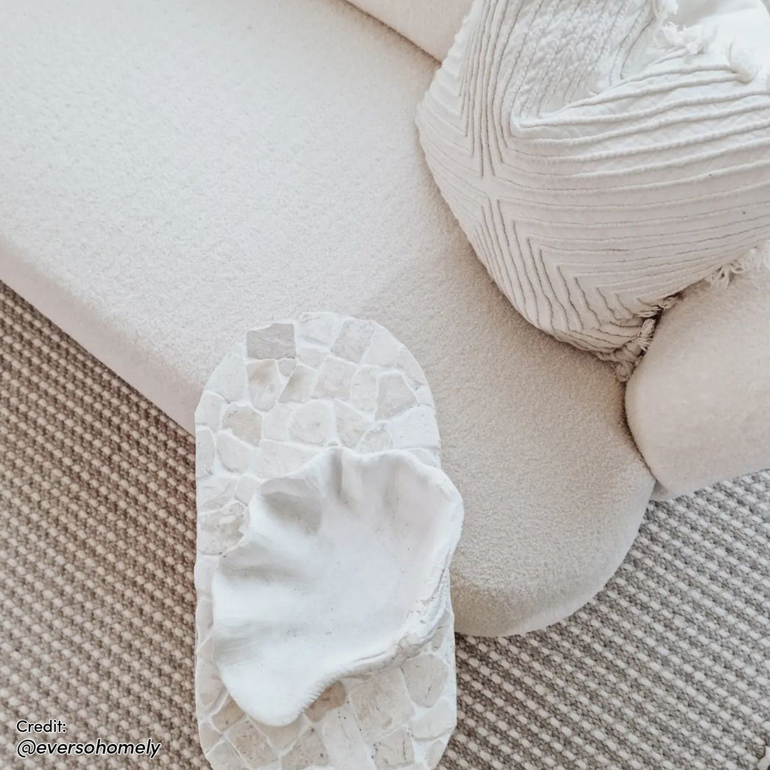 Massie 2-Seater Boucle Sofa in Cream White, featuring a low, rounded-corner design with plush boucle fabric, accompanied by a matching textured throw pillow and a sculptural coffee table with terrazzo-like detailing.