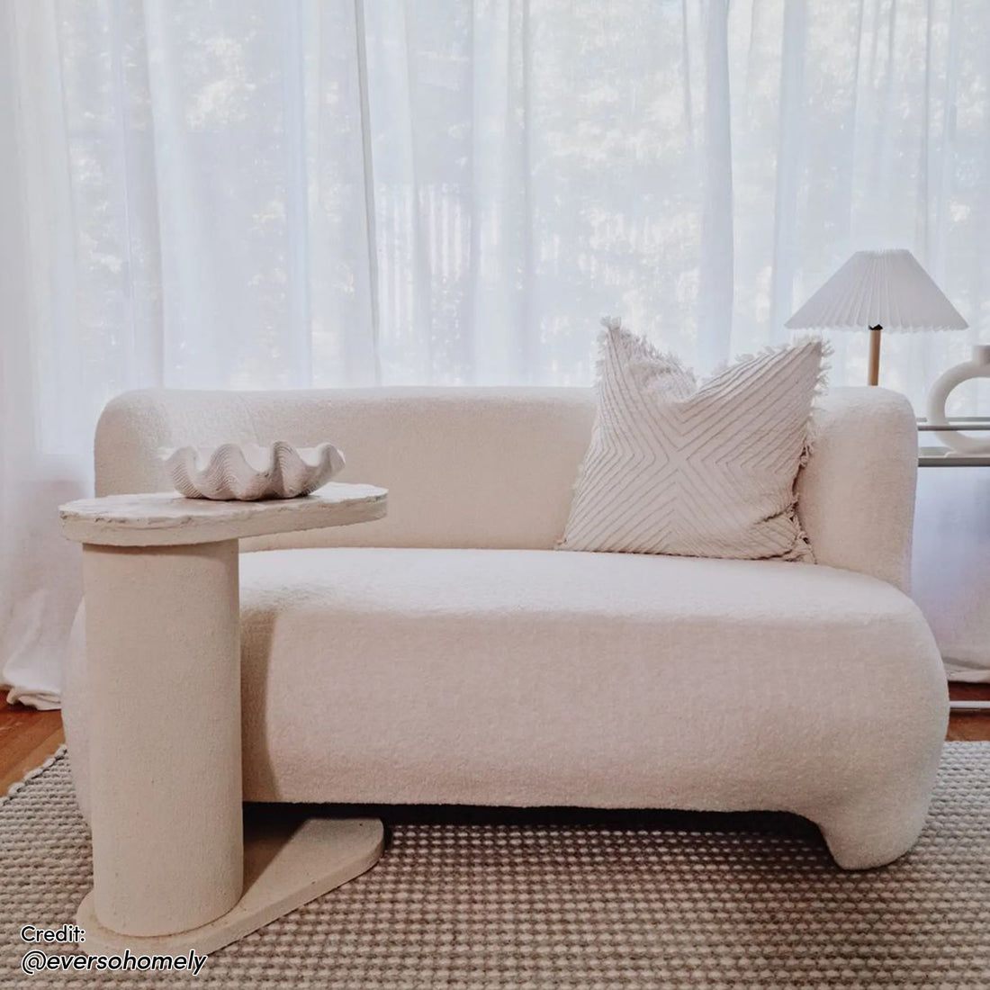 Massie 2-Seater Boucle Sofa in Cream White, featuring a curved design with plush boucle fabric and a built-in side table, set in a minimalist, softly lit living space.