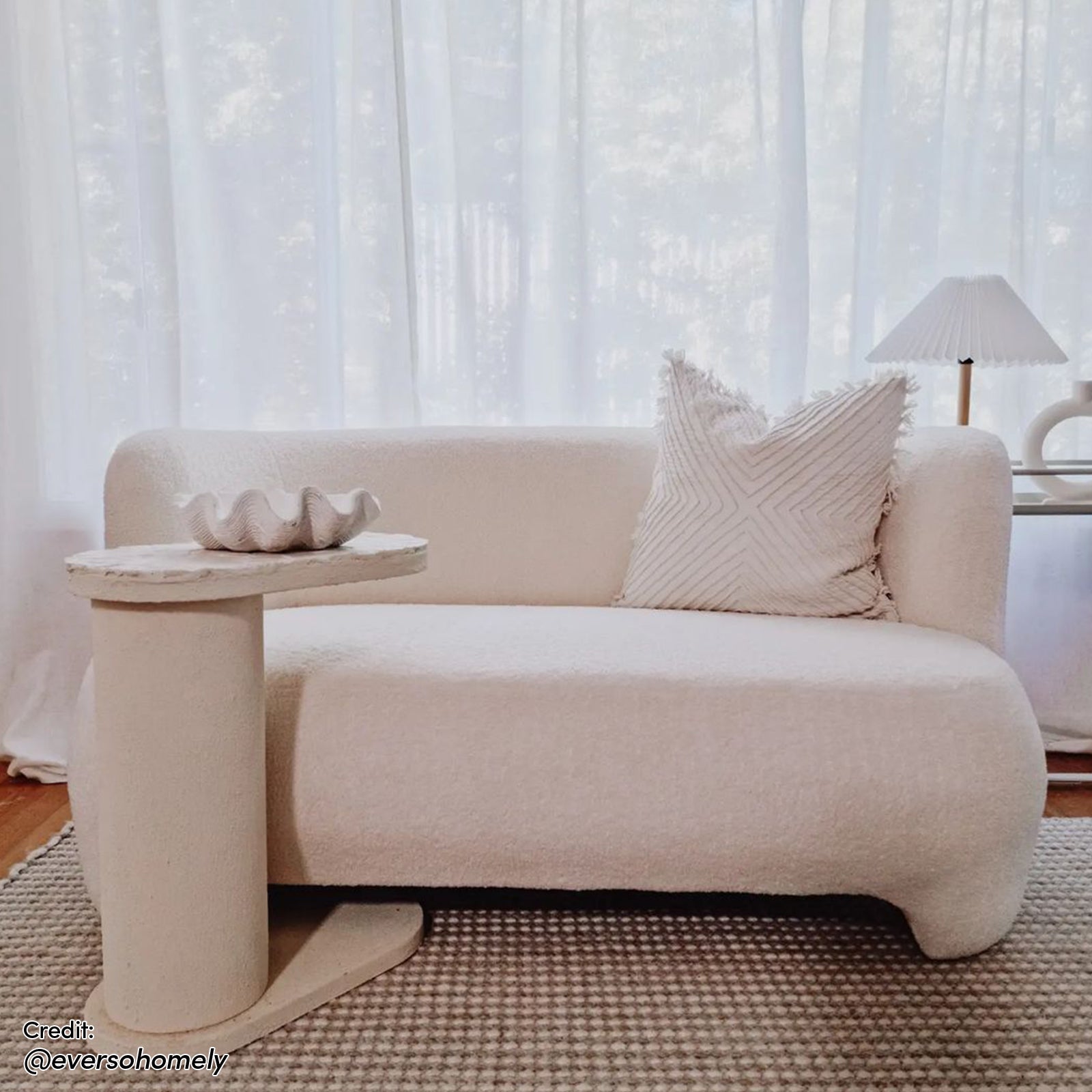 Massie 2-Seater Boucle Sofa in Cream White, featuring a curved design with plush boucle fabric and a built-in side table, set in a minimalist, softly lit living space.