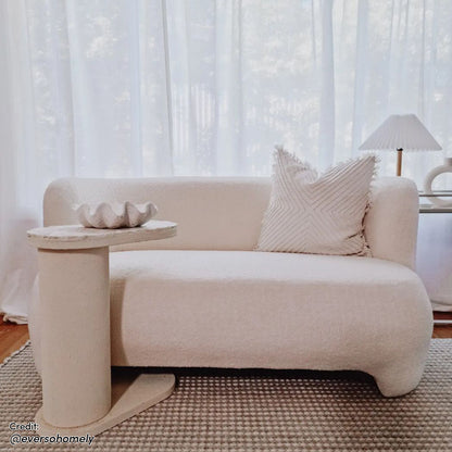 Massie 2-Seater Boucle Sofa in Cream White, featuring a curved design with plush boucle fabric and a built-in side table, set in a minimalist, softly lit living space.