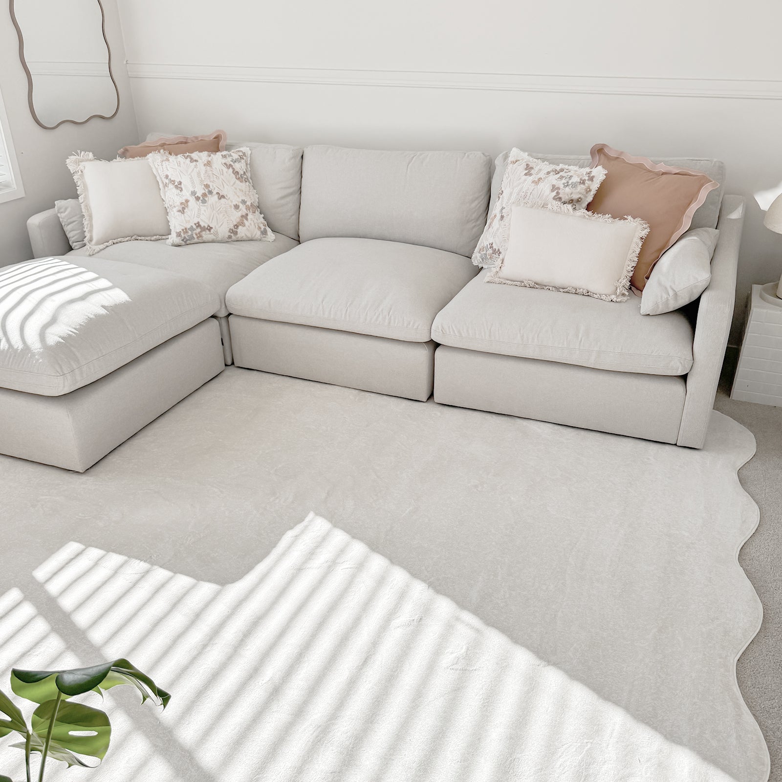 Millie 5-Seater Spill Resistant Fabric Sofa in Warm Light Grey features a low, L-shaped design with plush cushions, neutral-toned throw pillows, and a light rug beneath, creating a serene, minimalist living space.