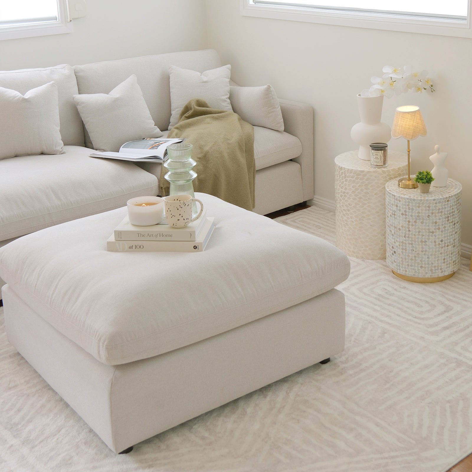 Millie Fabric Ottoman Modular Sofa Light Beige with a white ottoman, books, and a candle, showcasing its spacious, plush design and modular functionality in a stylish, comfortable living space setting.