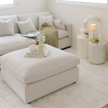 Millie Fabric Ottoman Modular Sofa Light Beige with a white ottoman, books, and a candle, showcasing its spacious, plush design and modular functionality in a stylish, comfortable living space setting.