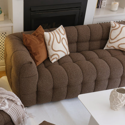 Norah 3 Seater Boucle Sofa in Brown, tufted and cozy with decorative pillows and a beige throw, anchored by a white coffee table and surrounded by a warm, inviting living room setting.