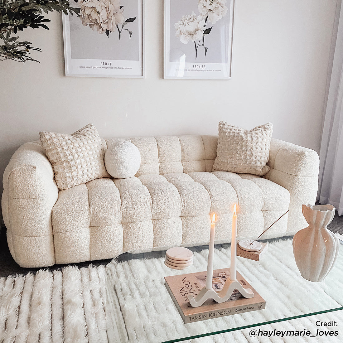 Norah 3 Seater Boucle Sofa in Cream White, featuring tufted square sections, two textured pillows, and a round cushion, placed in a serene, neutral-toned living room setting with modern decor elements.