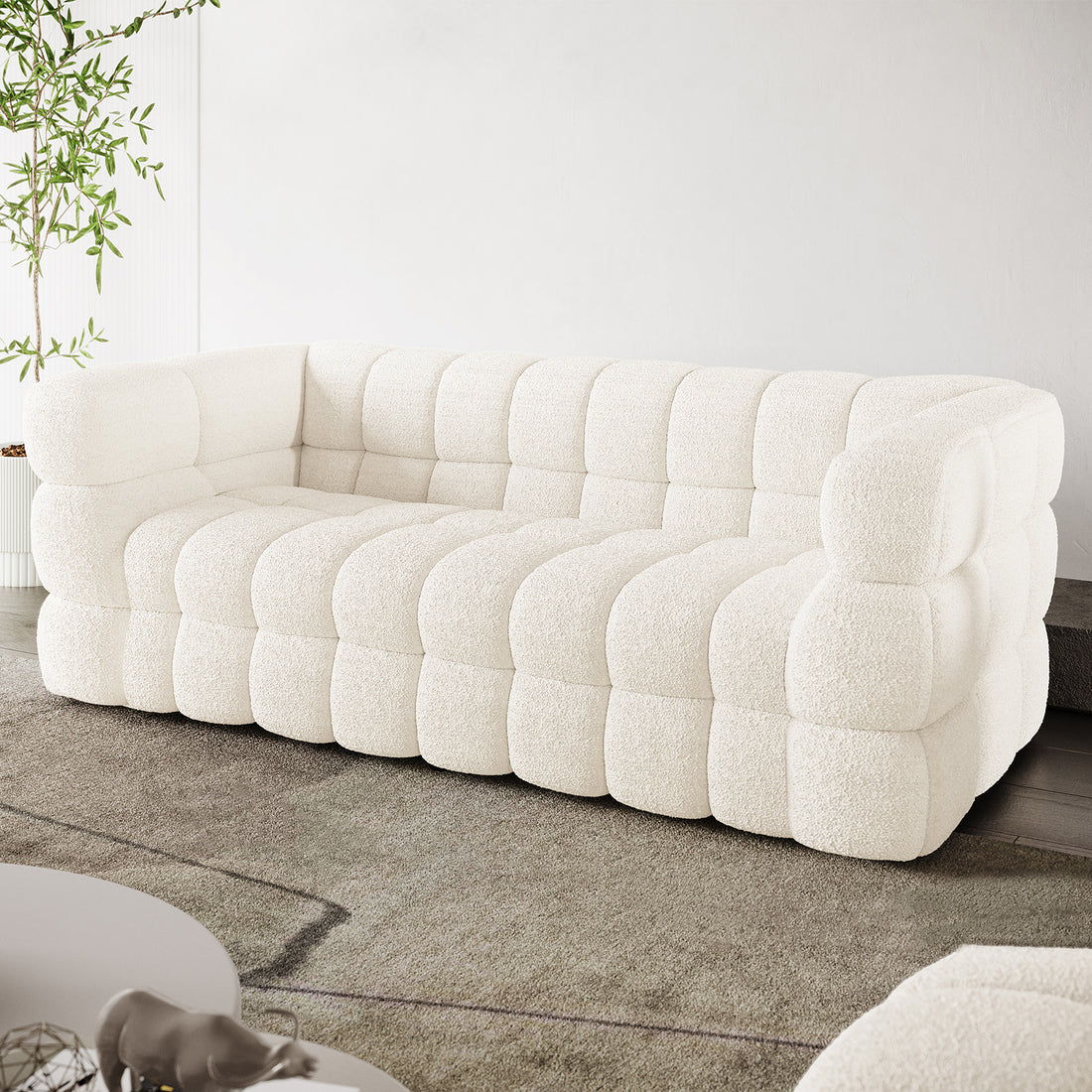 Norah 3 Seater Boucle Sofa in Cream White features a modular design with pillowy, tufted blocks, upholstered in off-white bouclé fabric, set in a bright, minimalist living room.