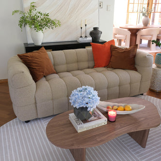 Norah 3 Seater Boucle Sofa in Warm Beige, featuring tufted, plush fabric with rust and brown throw pillows, set in a cozy living space with a wooden coffee table and decorative accents.