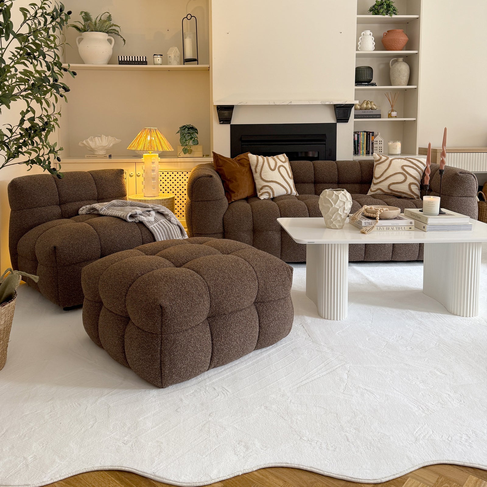 The Norah 5 Seater Boucle Sofa Set with Ottoman in Brown features a tufted armchair, ottoman, and two-seat sofa on a scalloped-edge rug, complemented by a sleek coffee table.