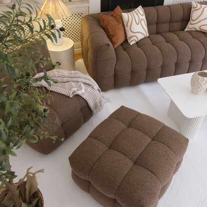 Norah 5 Seater Boucle Sofa Set With Ottoman in Brown, featuring quilted-style texture, rust-brown and cream pillows, atop a pale area rug, accompanied by a white coffee table and leafy plant.