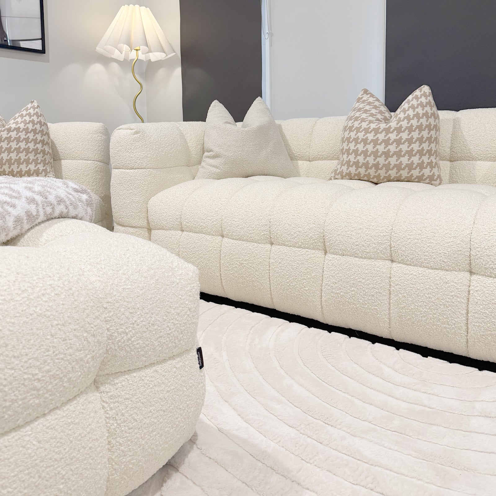 Norah 5 Seater Boucle Sofa Set with Ottoman in Cream White features a tufted ottoman and matching three-seat sofa with houndstooth and plain cushions, framed by dark window panels.