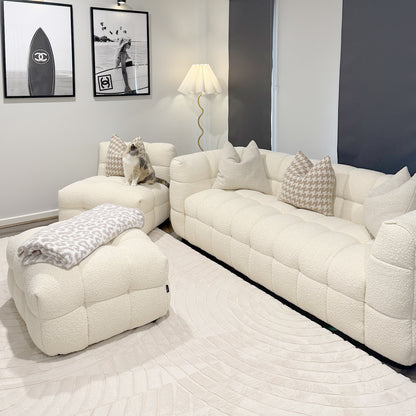 Norah 5 Seater Boucle Sofa Set with Ottoman in Cream White features a tufted design with matching ottoman, houndstooth-pattern pillows, and a light-beige blanket, creating a cozy, stylish living space.