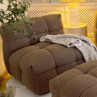 Norah Boucle Single Seater Sofa in Brown, featuring a deep-brown tufted design, is paired with a matching ottoman, accented by a textured throw and adjacent to a mosaic-topped side table.