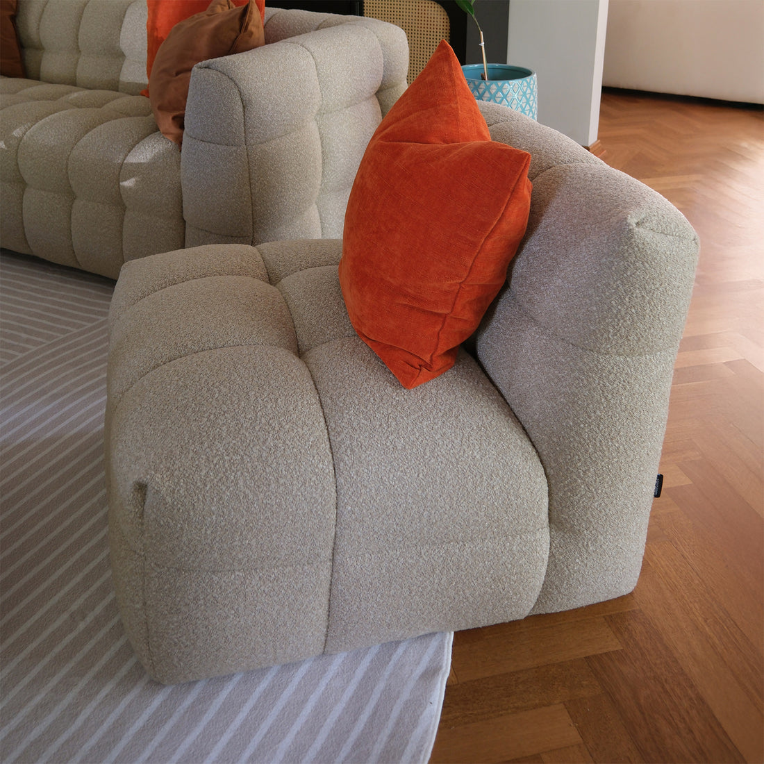 Norah Boucle Single Seater Sofa in Warm Beige, featuring textured off-white bouclé upholstery, deep cushioning, and a burnt-orange throw pillow, sits on a light-striped area rug with a herringbone hardwood floor.