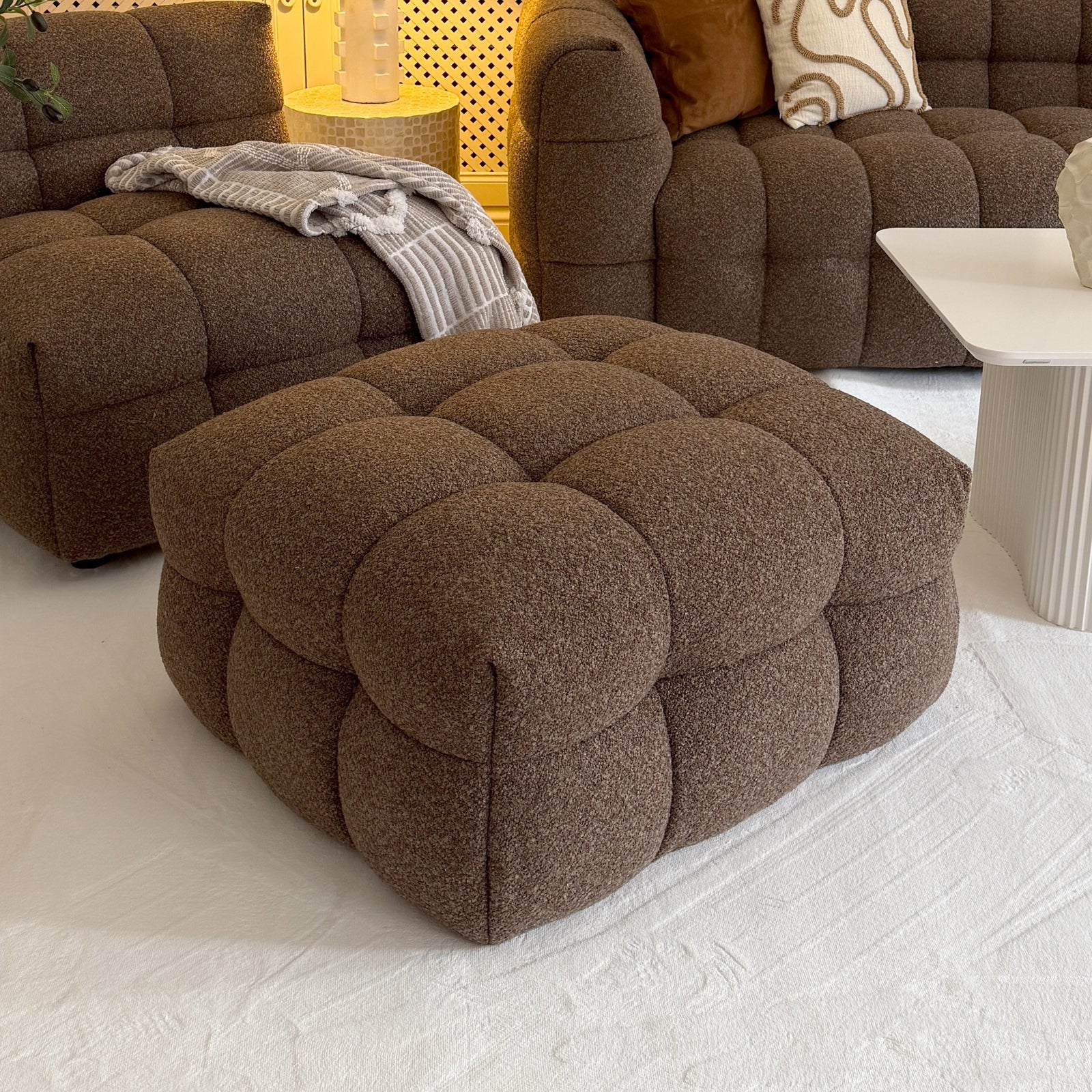 Norah Boucle Ottoman in Brown, a large square tufted piece in cozy bouclé fabric, complements the matching seating area, providing stylish versatility as a footrest or chic coffee table alternative.