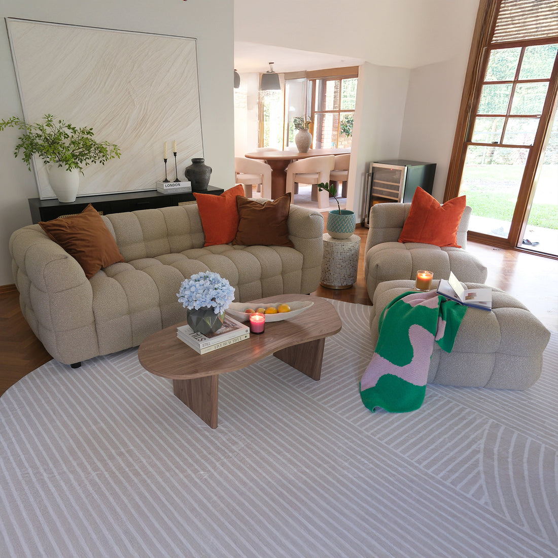 Norah 5 Seater Boucle Sofa Set with Ottoman in Warm Beige featuring a plush tufted design, rust-orange and brown pillows, alongside a matching armchair and ottoman with an abstract-patterned throw.