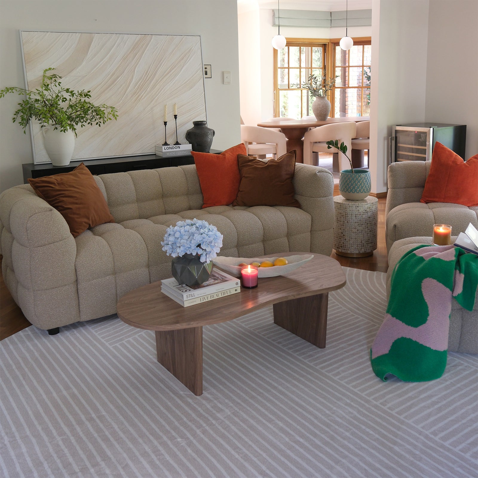 Norah 5 Seater Boucle Sofa Set With Ottoman in Warm Beige, features tufted upholstery, accent pillows, and a draped throw, positioned in a bright living room with a wooden coffee table and decorative elements.