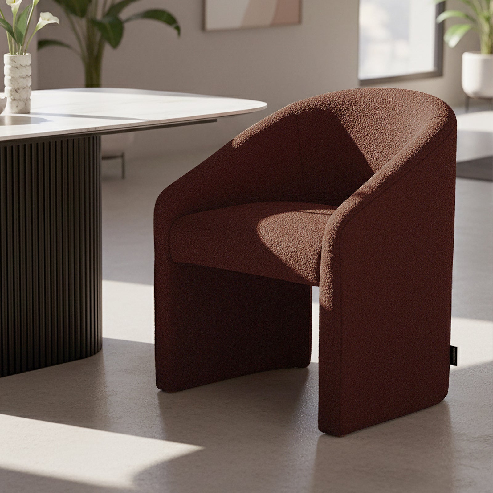 Nuve Bouclé Upholstered Accent Armchair in Rust Brown, features a modern, curved design with rich, textured fabric, set on a light floor beside a table with fluted detailing.