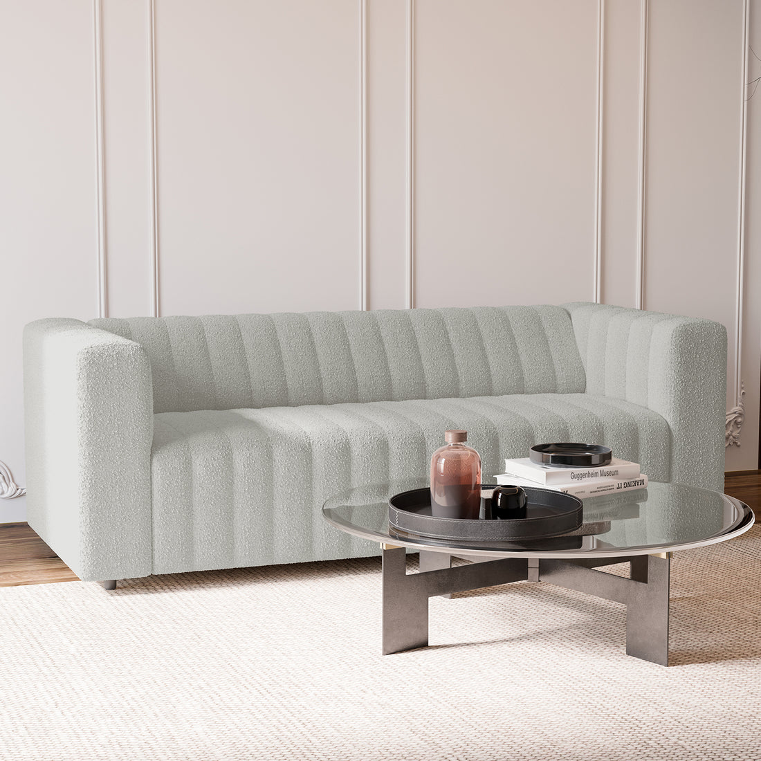 Parisa 3 Seater Tufted Boucle Sofa in Light Grey, featuring a low-rise, channel-tufted design, is centered against a paneled wall, paired with a round glass coffee table and decorative accents.