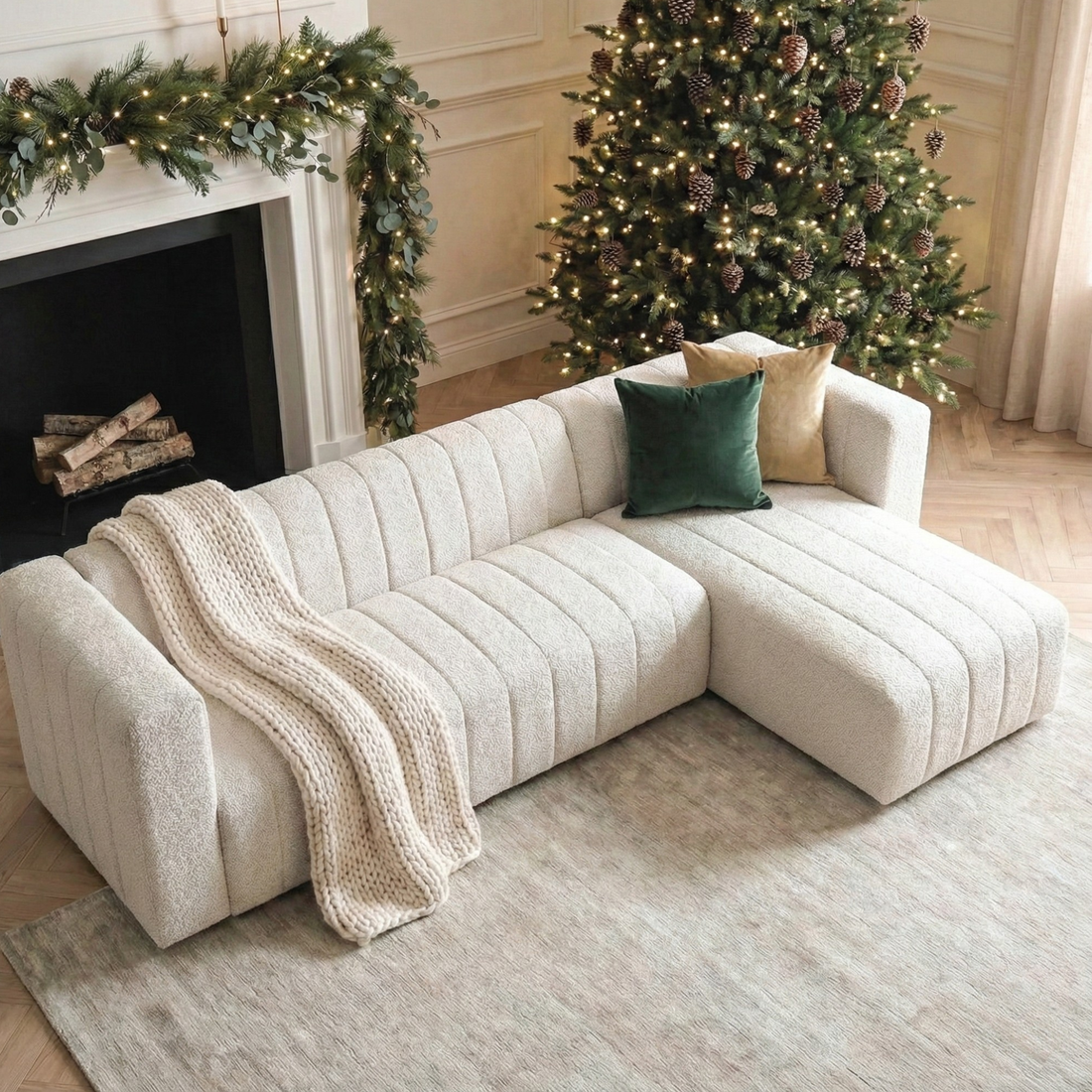 Parisa 4 Seater Tufted Boucle Sofa with Chaise in Cream White, featuring vertical channel tufting and deep seating, is adorned with a chunky knit throw and two accent pillows.