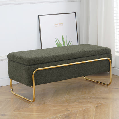 Riane Boucle Storage Ottoman in Green features a rectangular design with boucle upholstery and gold U-shaped legs, set on a wood floor, complemented by a plant-themed print in the background.