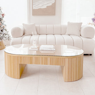 The Samira 3 Seater Velvet Sofa in Cream features plush channel tufting, cylindrical bolster arms, and matching throw pillows, set in a minimalist living room with a light wood slat coffee table.