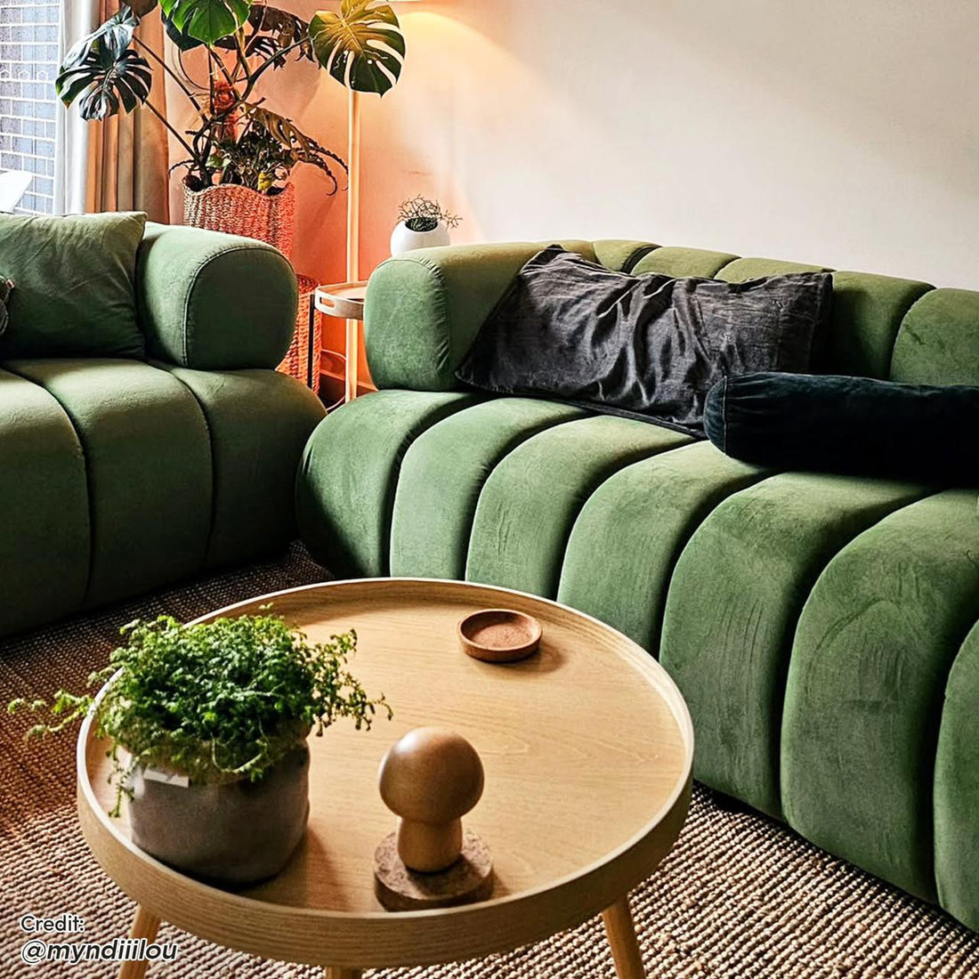 Samira 5 Seater Velvet Sofa Set in Prasinous Green features deep-green, channel-tufted sofas with rounded arms, topped with dark lumbar cushions, in a cozy living-room setting with natural accents.