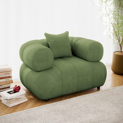 Samira Single Seater Velvet Sofa in Prasinous Green, featuring soft green upholstery, thick armrests, and a matching pillow, set on a herringbone floor with books and a potted plant nearby.
