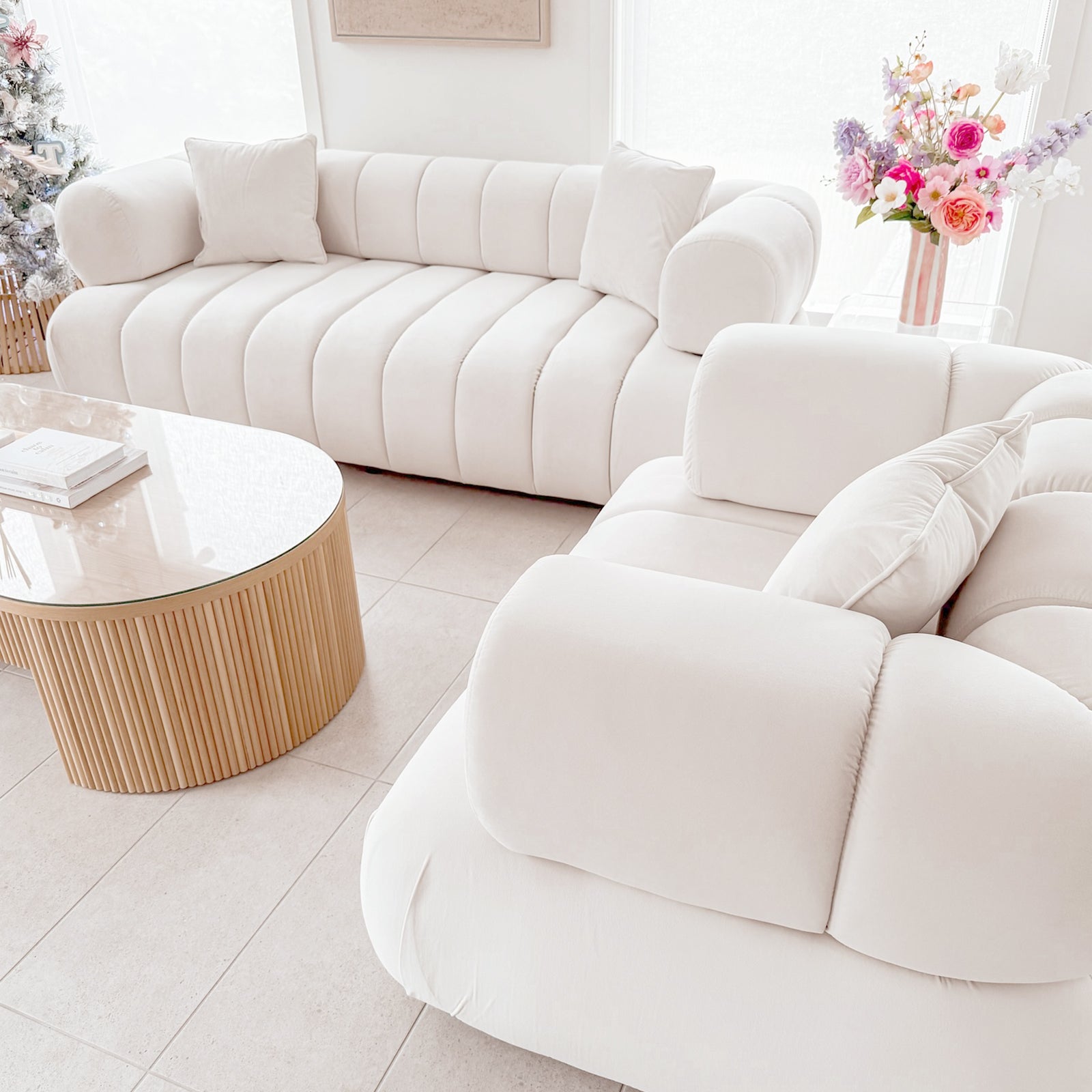 Samira 6 Seater Velvet Sofa Set in Cream features channel-tufted upholstery facing each other, with matching pillows and a round glass-top coffee table between them, creating an inviting, elegant living space.
